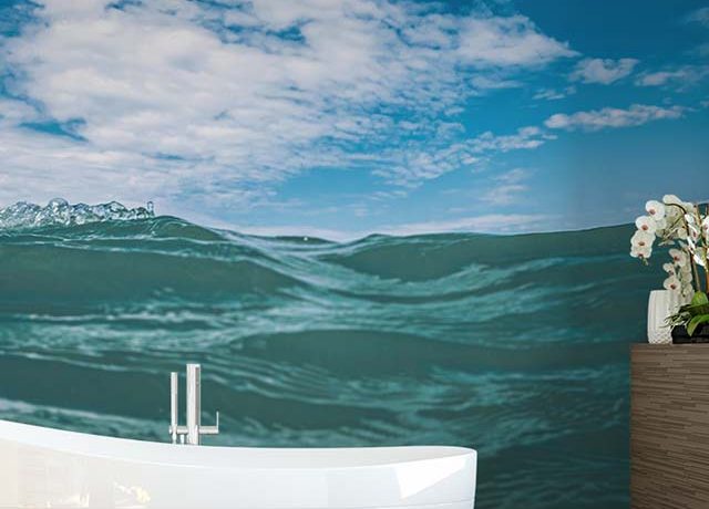 A serene ocean wave and blue sky Bathroom Wallpaper behind a modern white bathtub and vanity with an orchid plant.