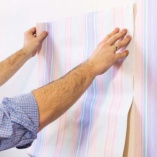 a-person-aligns-and-installs-striped-wallpaper-featuring-blue-wallpaper-patterns-on-a-wall A person aligns and installs striped wallpaper featuring blue wallpaper patterns on a wall.