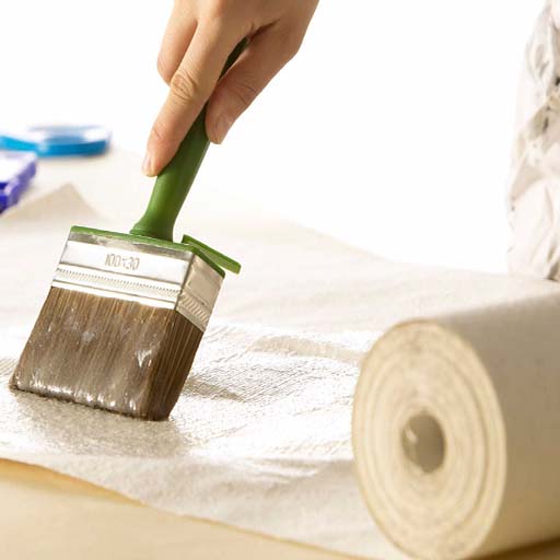 a-person-applies-adhesive-with-a-brush-to-wallpaper-preparing-to-install-blue-wallpaper-patterns A person applies adhesive with a brush to wallpaper, preparing to install blue wallpaper patterns.