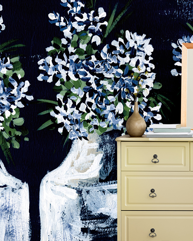 A room with a floral blue wallpaper featuring white blossoms, highlighting blue wallpaper trends, and a beige cabinet with a vase