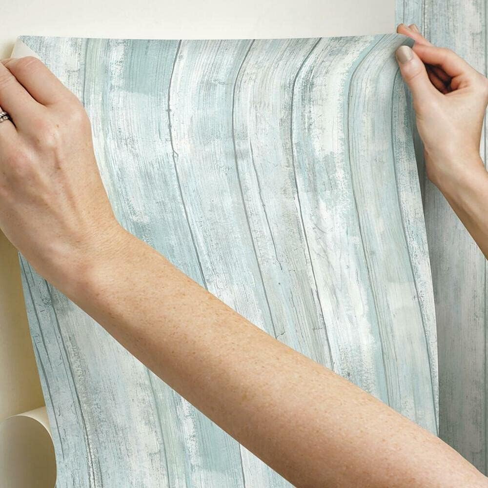 hands-applying-a-textured-blue-wallpaper-with-subtle-woodgrain-effect-showcasing-popular-blue-wallpaper-textures Hands applying a textured blue wallpaper with subtle woodgrain effect, showcasing popular blue wallpaper textures.