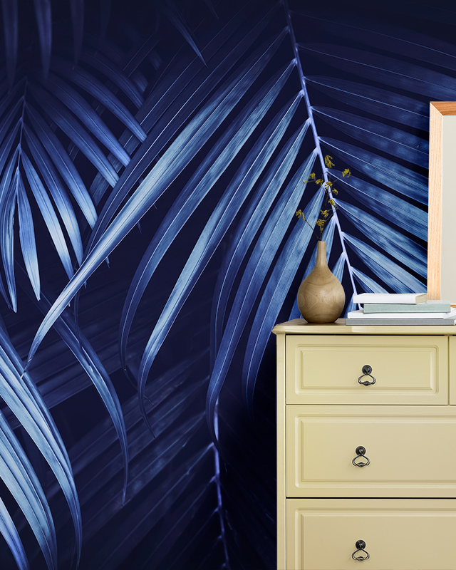 Room with tropical-themed blue wallpaper trends featuring palm leaves, and a beige dresser with books and a vase