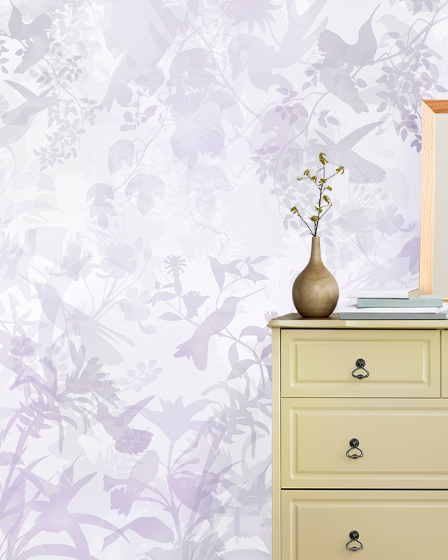 Floral Wallpaper Trend featuring subtle lavender silhouettes of birds and flowers. In front of the wallpaper is a beige dresser with a vase and stacked books. Floral Wallpaper Trend featuring subtle lavender silhouettes of birds and flowers. In front of the wallpaper is a beige dresser with a vase and stacked books.