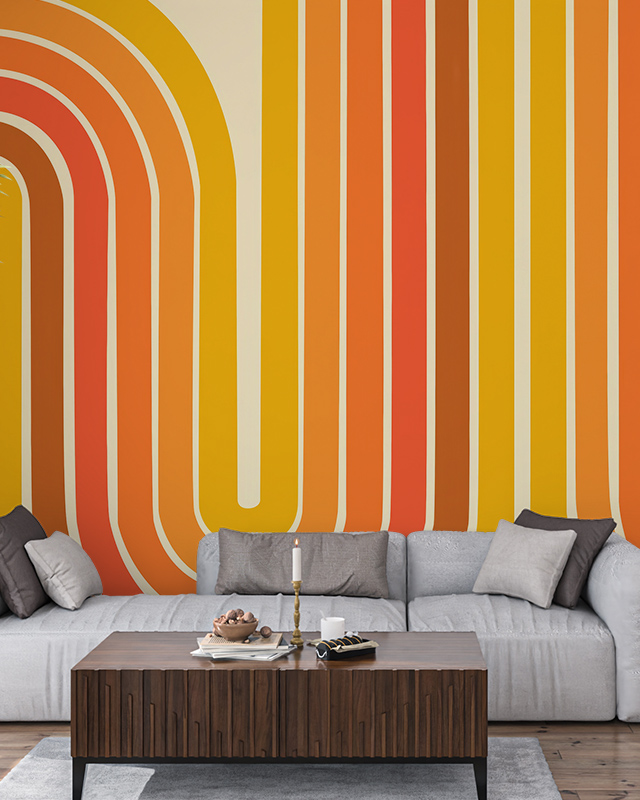 Vibrant orange and yellow abstract wallpaper installation behind a modern gray sofa and wooden coffee table