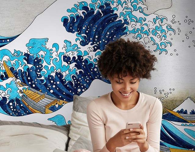Woman sitting in front of a vibrant wave-themed mural, showcasing Wallpaper Installation in a cozy bedroom.