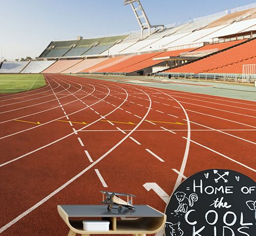 A track and field stadium-themed wallpaper, ideal as sports wallpaper for man caves, with a kids' desk in front.