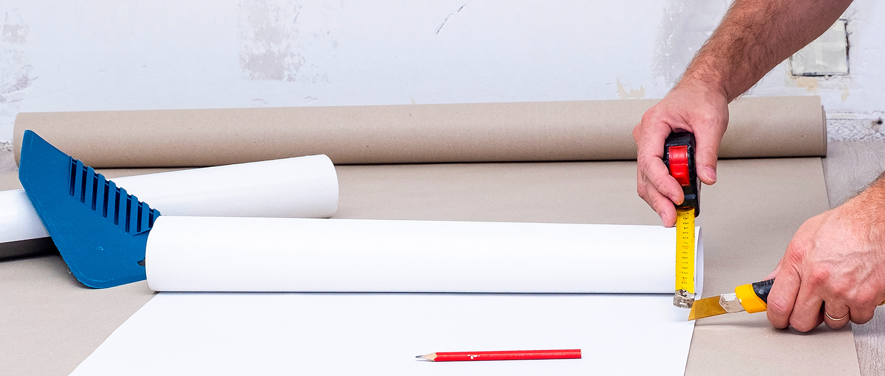 Close-up of tools and hands measuring and cutting wallpaper during a wallpaper installation