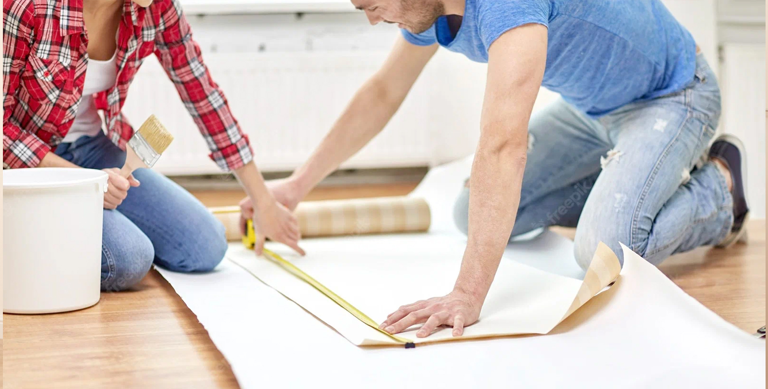 a-couple-measuring-and-preparing-to-cut-wallpaper-for-installation-highlighting-steps-for-installing-peel-and-stick-wallpaper A couple measuring and preparing to cut wallpaper for installation, highlighting steps for installing peel and stick wallpaper.