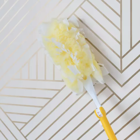 a-duster-cleaning-geometric-peel-and-stick-wallpaper-showing-easy-maintenance-after-installing-peel-and-stick-wallpaper A duster cleaning geometric peel and stick wallpaper, showing easy maintenance after installing peel and stick wallpaper.