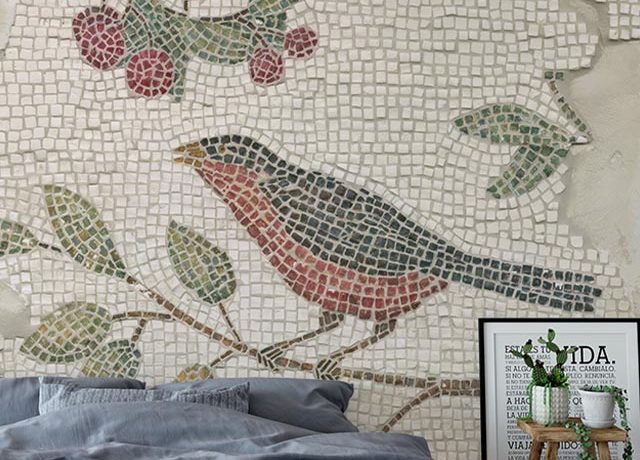 A mosaic-style bird design on peel and stick wallpaper behind a cozy bed, highlighting peel and stick wallpaper trends.