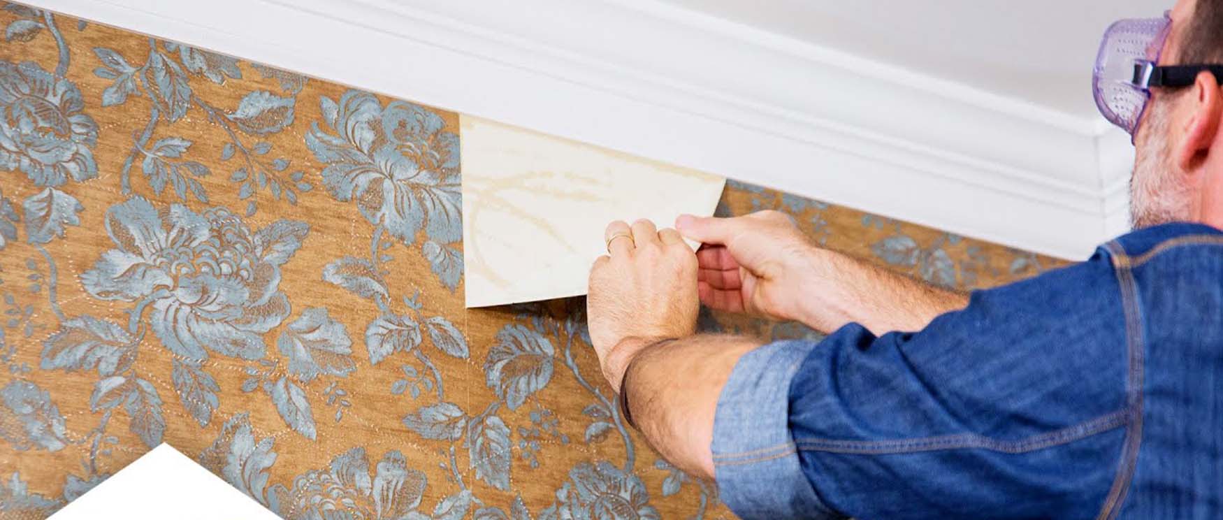 a-person-is-carefully-using-their-hands-to-remove-removable-wallpaper-with-a-blue-floral-pattern-from-the-wall A person is carefully using their hands to remove removable wallpaper with a blue floral pattern from the wall.