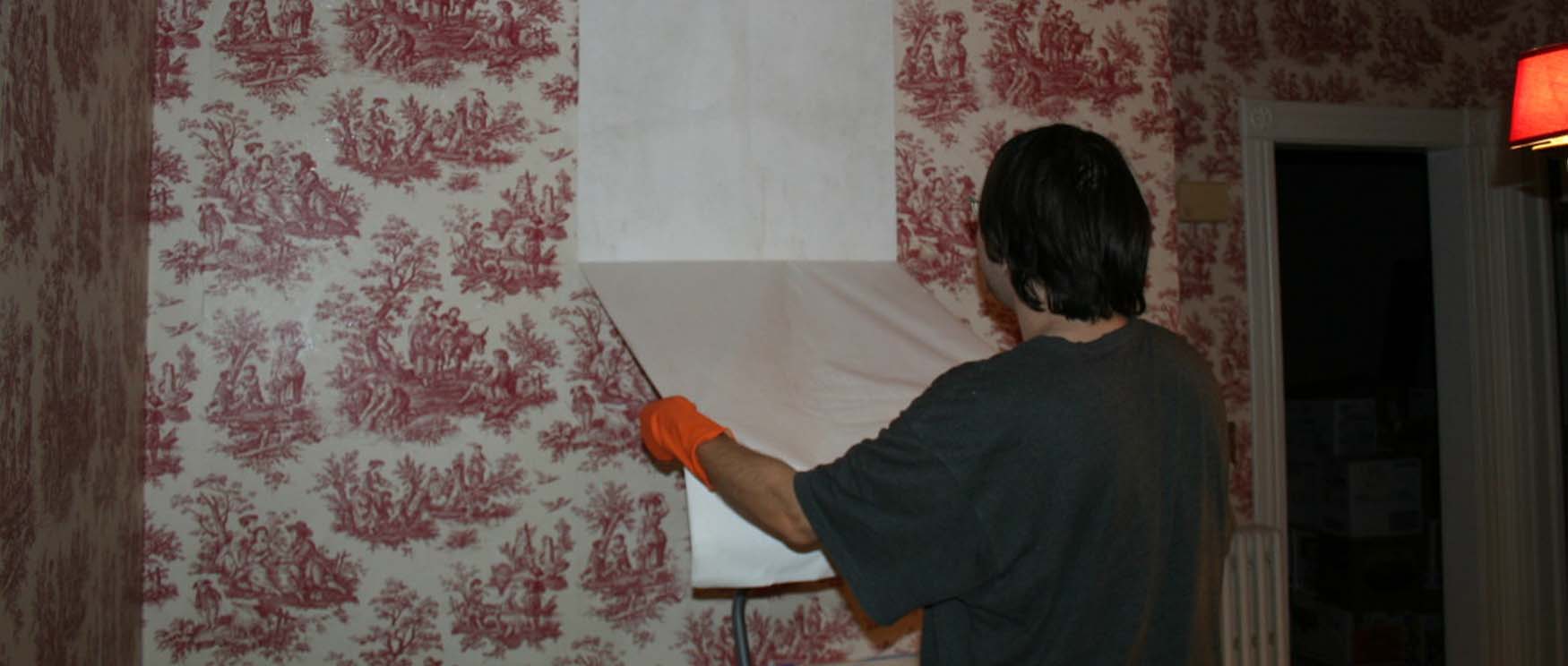 a-person-is-using-gloves-to-remove-removable-wallpaper-with-a-red-pattern-from-the-wall A person is using gloves to remove removable wallpaper with a red pattern from the wall.