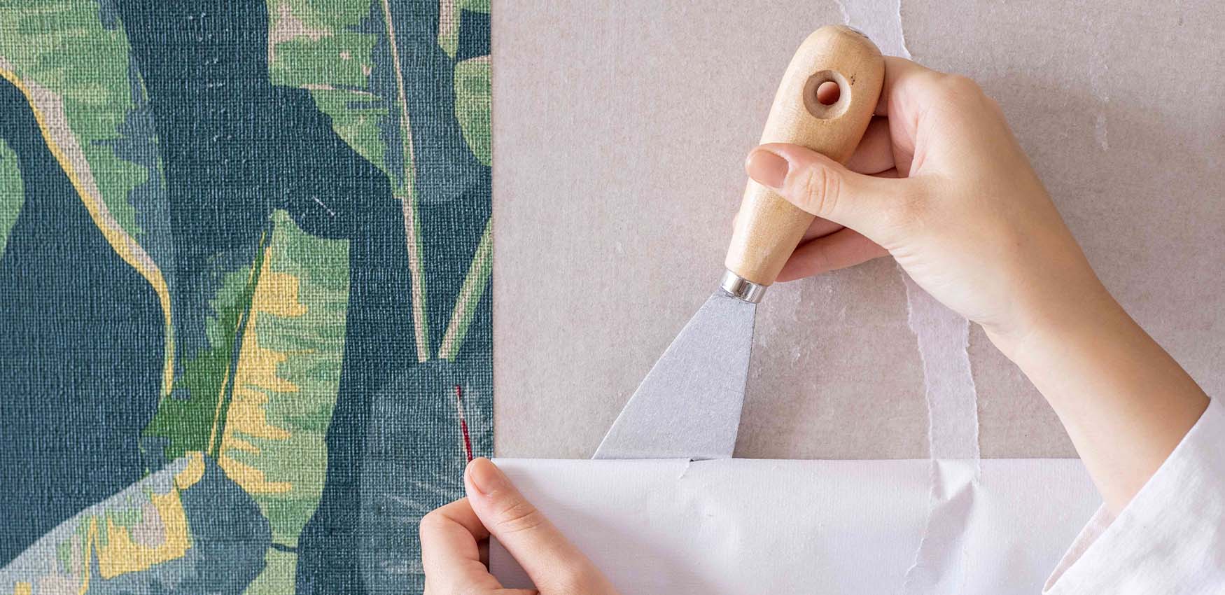 a-person-uses-a-scraper-to-peel-off-tropical-themed-wallpaper-illustrating-the-pros-and-cons-of-removable-wallpaper A person uses a scraper to peel off tropical-themed wallpaper, illustrating the Pros and Cons of Removable Wallpaper.