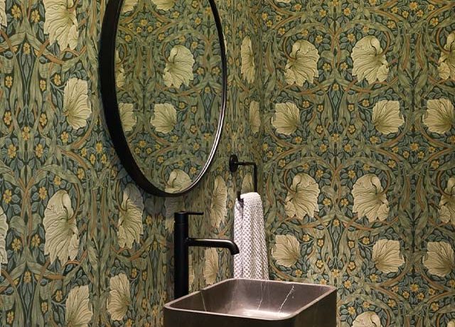 Bathroom with William Morris wallpaper in Modern Homes featuring floral design, round mirror, black sink, and towel.