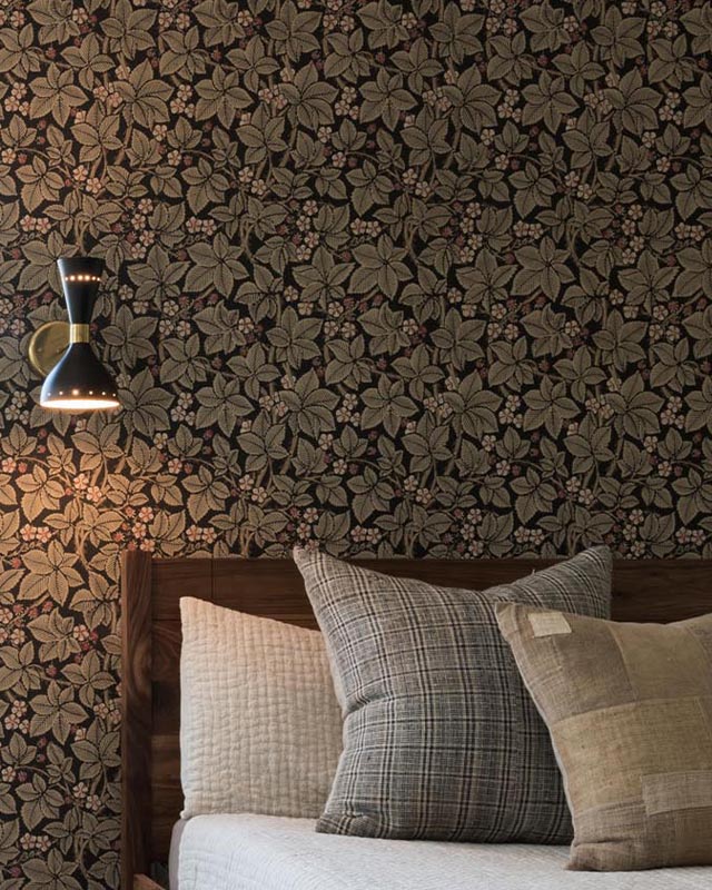 bedroom-with-dark-floral-william-morris-wallpaper-patterns-plaid-pillows-and-a-modern-black-wall-mounted-light-fixture Bedroom with dark floral William Morris wallpaper patterns, plaid pillows, and a modern black wall-mounted light fixture.