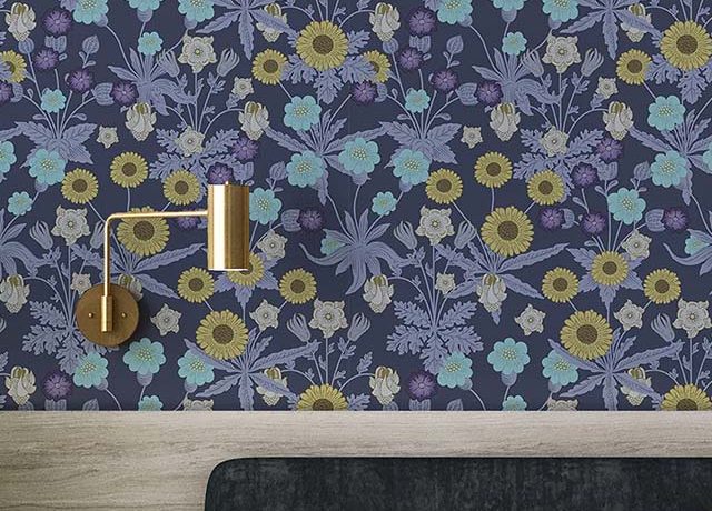 Dark floral wallpaper with yellow, blue, and purple flowers, William Morris vs. Modern Wallpaper Styles behind bed and gold lamp.