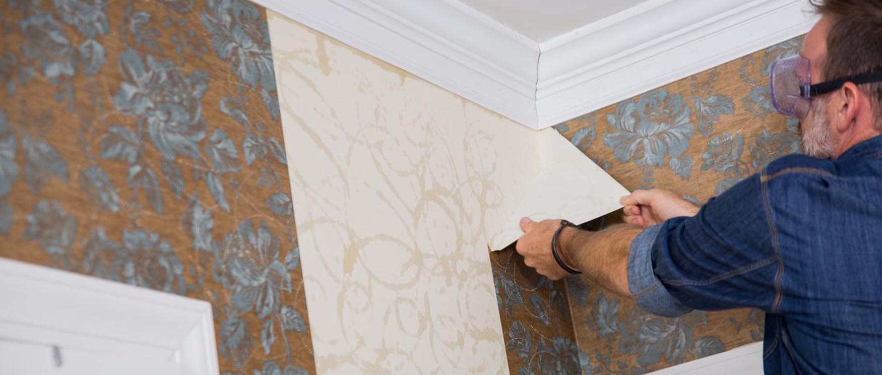 man-carefully-peeling-off-floral-patterned-wallpaper-demonstrating-the-removal-of-peel-and-stick-wallpaper Man carefully peeling off floral-patterned wallpaper, demonstrating the removal of peel and stick wallpaper.