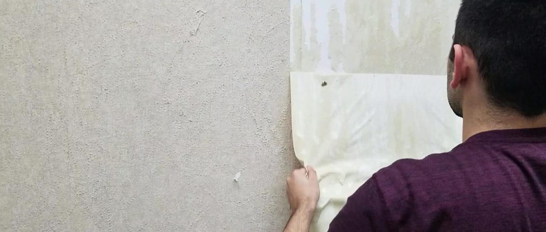 man-peeling-off-a-sheet-of-wallpaper-demonstrating-the-removal-of-peel-and-stick-wallpaper-from-a-wall Man peeling off a sheet of wallpaper, demonstrating the removal of peel and stick wallpaper from a wall.