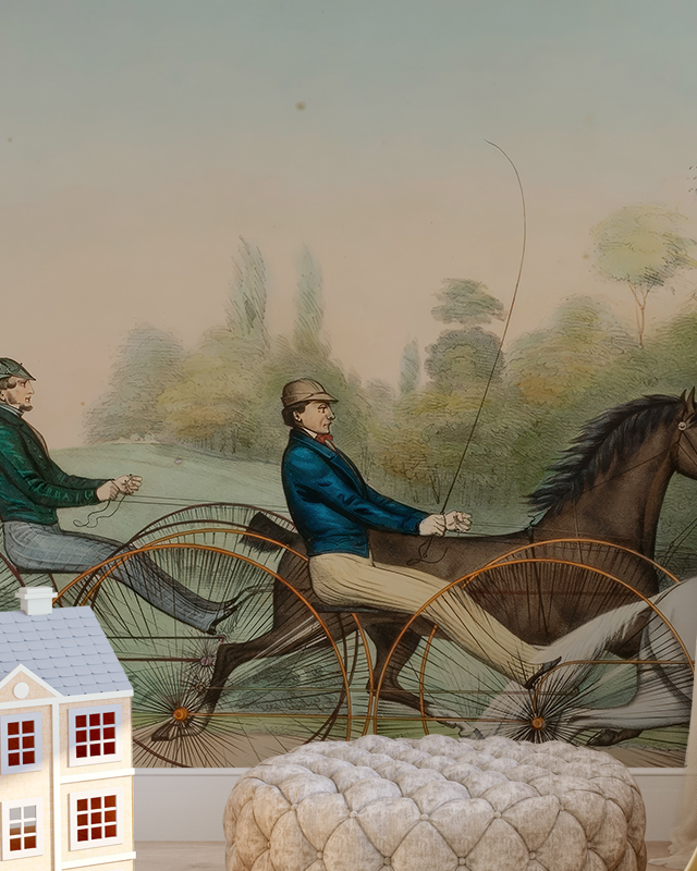 Vintage wallpaper for small spaces featuring horse-drawn carriages, with a toy house and pouf in the foreground.