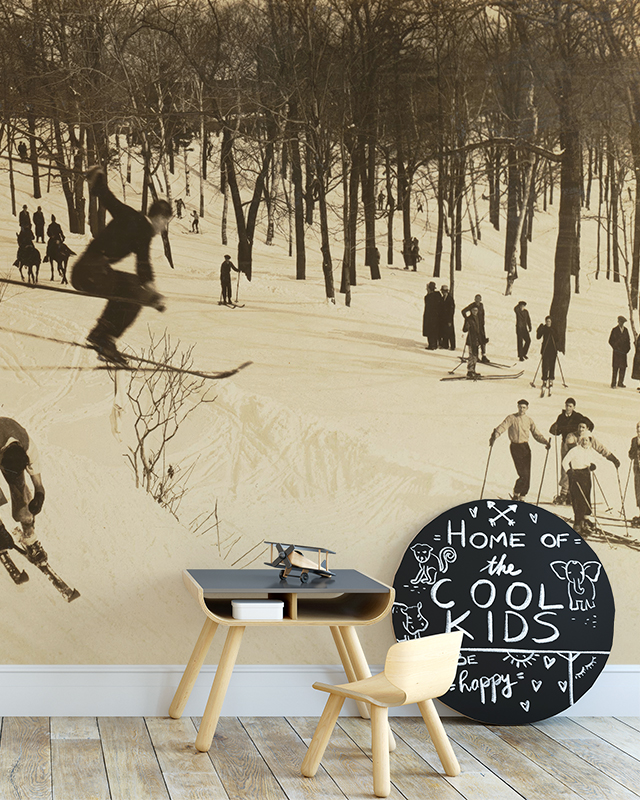 vintage-wallpapers-for-large-spaces-featuring-a-sepia-toned-skiing-scene-behind-a-small-children-s-desk-and-chair Vintage wallpapers for large spaces featuring a sepia-toned skiing scene, behind a small children's desk and chair.