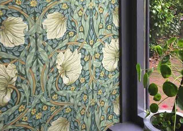 William Morris wallpaper patterns with green floral designs beside a window and a potted plant on the windowsill.