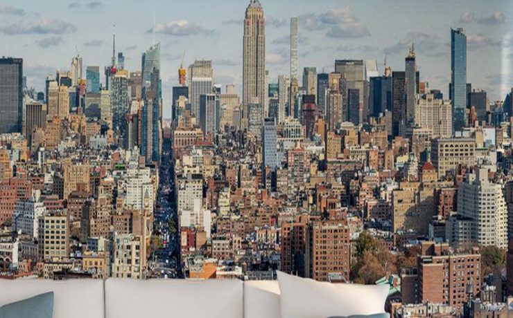 A vibrant city skyline mural behind a white sofa with cushions and a vase, showcasing urban wallpaper for different room types.