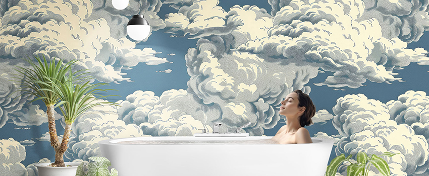 Woman relaxing in a bathtub against a cloud-themed blue wallpaper background. 