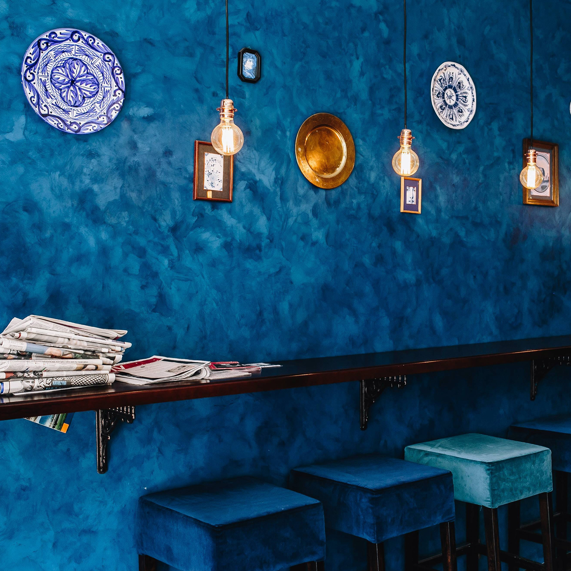 Stylish bar interior featuring textured blue wallpaper, blue velvet bar stools, and hanging pendant lights with warm lighting 