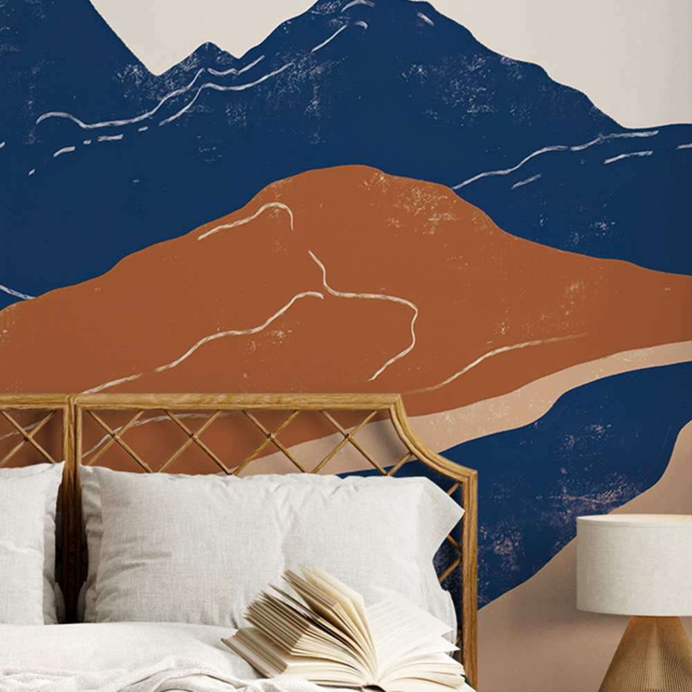 Mountain silhouette in blue wallpaper behind bed with wicker headboard and open book 