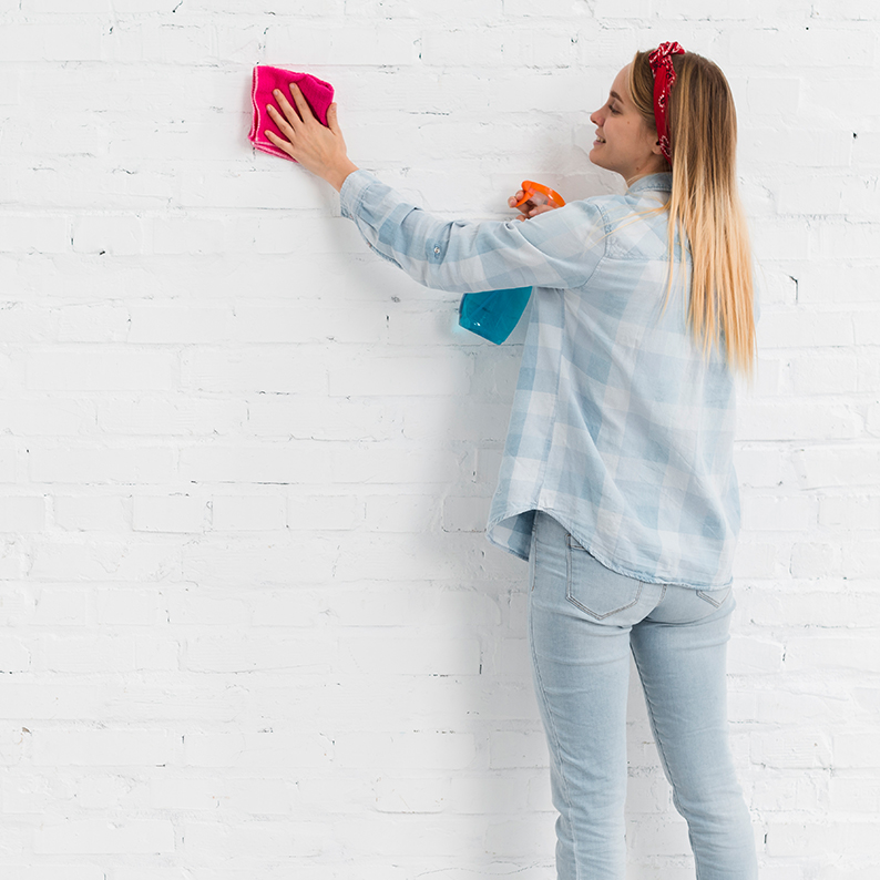 A woman cleaning wallpaper near a wall featuring a white brick design with a pink sponge, 